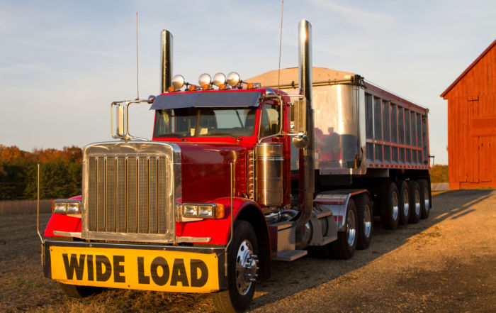 Common Injuries Following a Truck Crash - Tractor trailor with wide load sign is parked in front of a barn in the late afternoon sun.